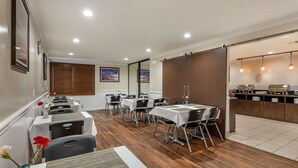 Uma sala de jantar com mesas e cadeiras, uma cozinha com armários e eletrodomésticos, e vista para o exterior.