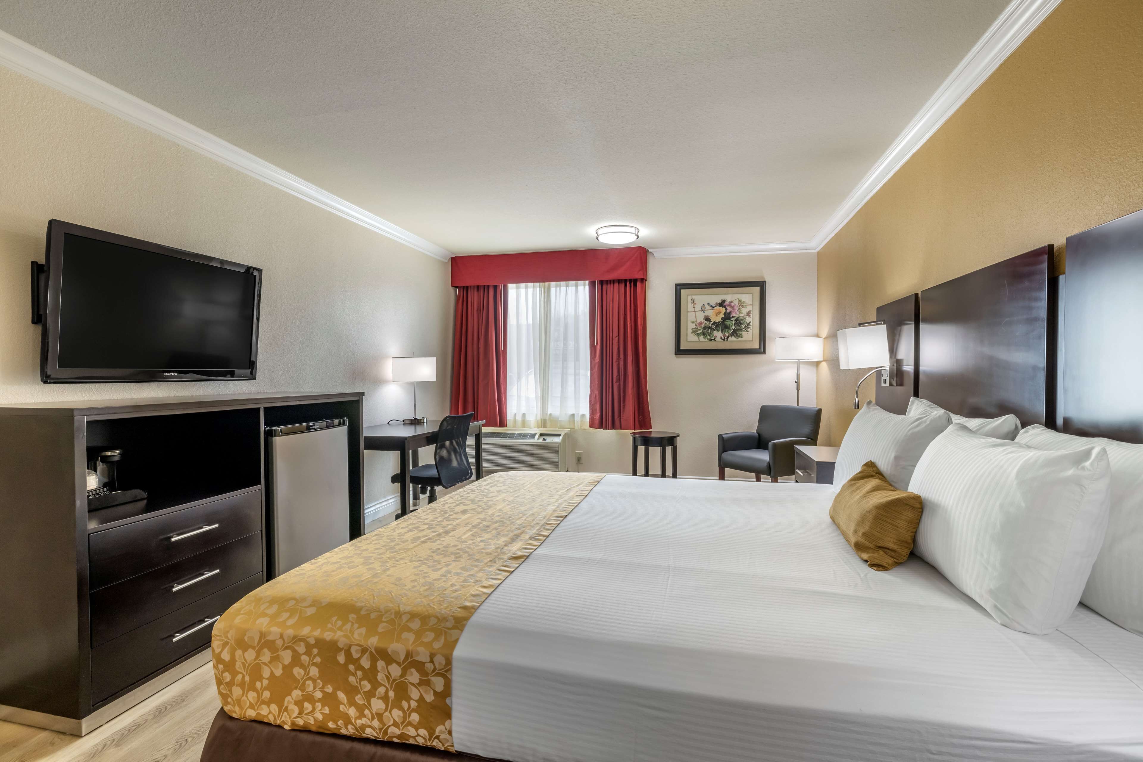 Une chambre d’hôtel avec un lit, un bureau, une télévision et une fenêtre avec des rideaux rouges.