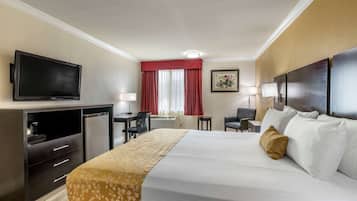 A hotel room with a bed, a desk, a television, and a window with red curtains.