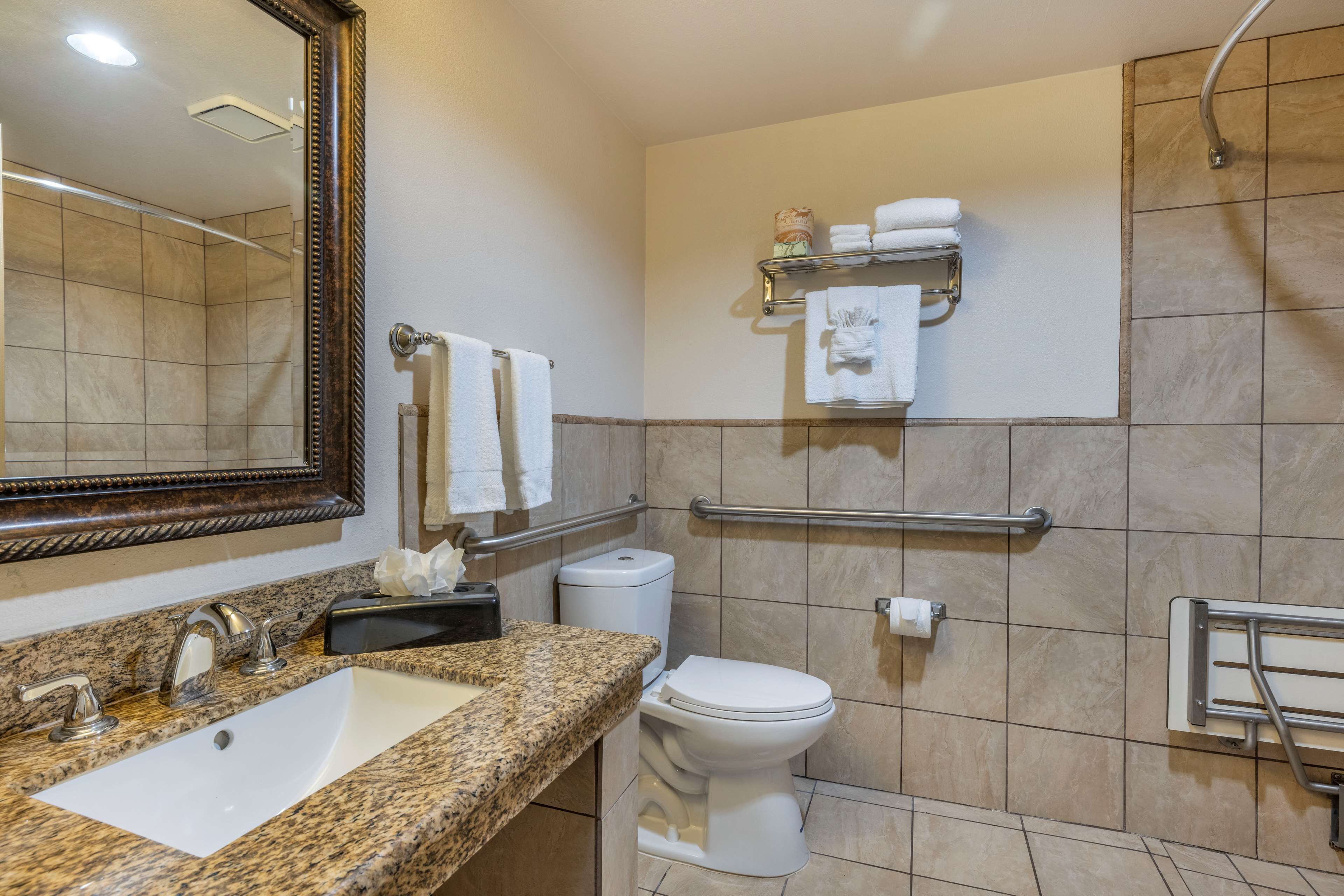 A bathroom with a granite countertop sink, a white toilet, a mirror, and a towel rack with towels.