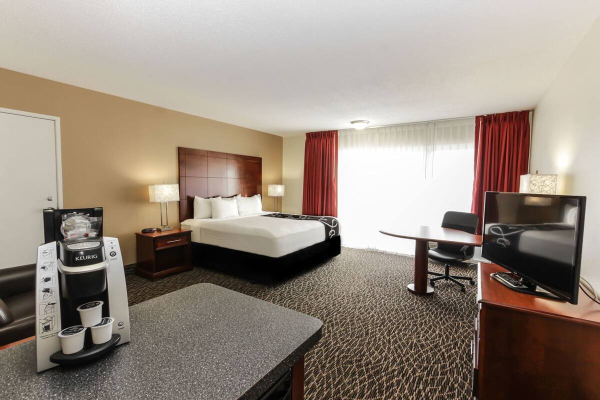 Habitación de hotel con cama, cafetera, televisión, escritorio y una silla.