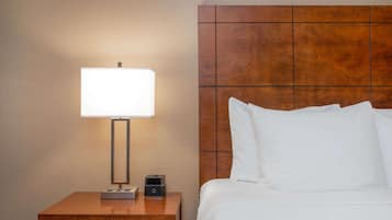 A neatly made bed with white linens, a wooden nightstand with a lamp and a small electronic device, and a wooden headboard.