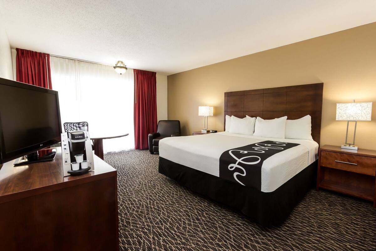 Una habitación de hotel con cama, televisión, cafetera, escritorio y lámpara.