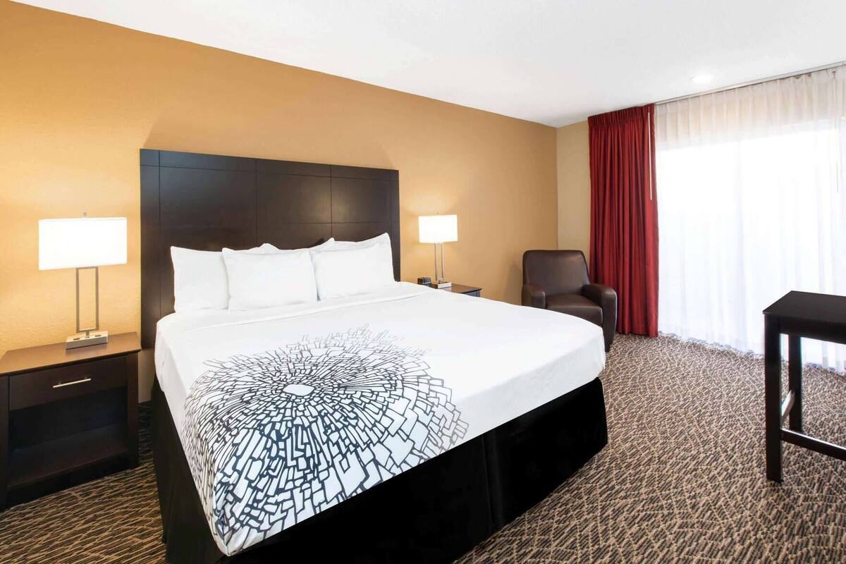 Una habitación de hotel con una cama grande, dos mesitas de noche con lámparas, una silla y un escritorio.