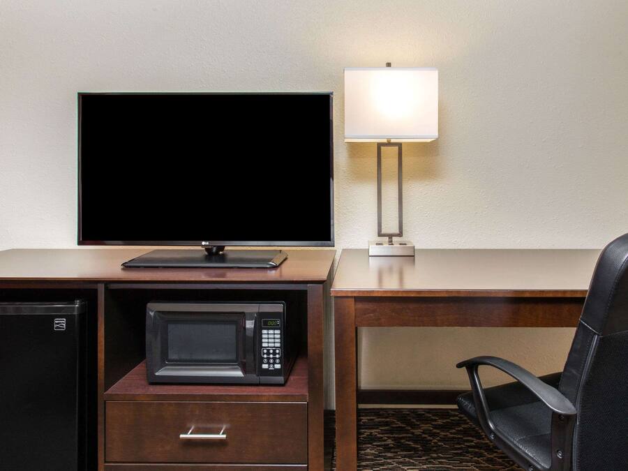 A hotel room with a desk, a television, a microwave, a lamp, a chair, and a mini fridge.