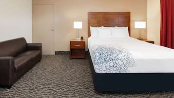 A hotel room with a large bed, two bedside tables, a brown leather sofa, and a patterned carpet.