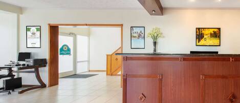 A reception area with a wooden reception desk, a computer on a desk, framed certificates on the wall, and a sign reading "la Quinta".