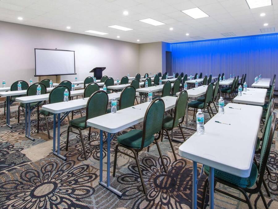 A conference room with rows of tables and chairs, a projector screen, and a podium.