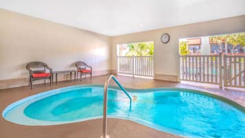 Uma piscina interior com uma escada de metal, duas cadeiras de vime com almofadas vermelhas e um relógio na parede.