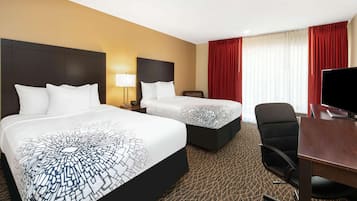 Une chambre d’hôtel avec deux lits, un bureau, une chaise, une télévision et une fenêtre avec des rideaux.