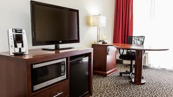 Habitación de hotel con televisión de pantalla plana, cafetera, microondas, refrigerador minibar, mesa de comedor con una silla y una lámpara.