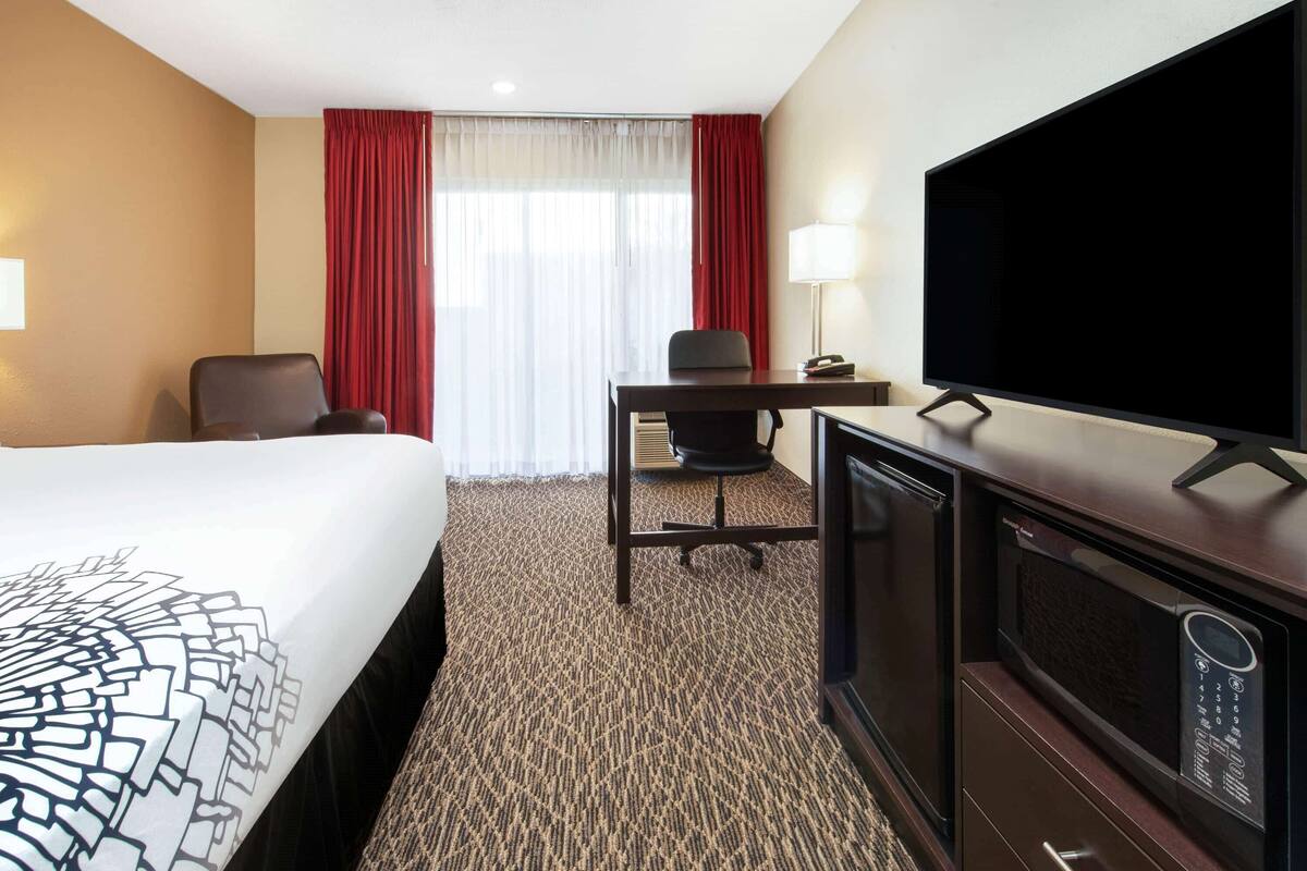 Una habitación de hotel con cama, escritorio, silla, televisor y microondas.