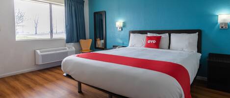 Une chambre d’hôtel avec un grand lit, une fenêtre avec des rideaux, un miroir fixé au mur et une table de chevet.