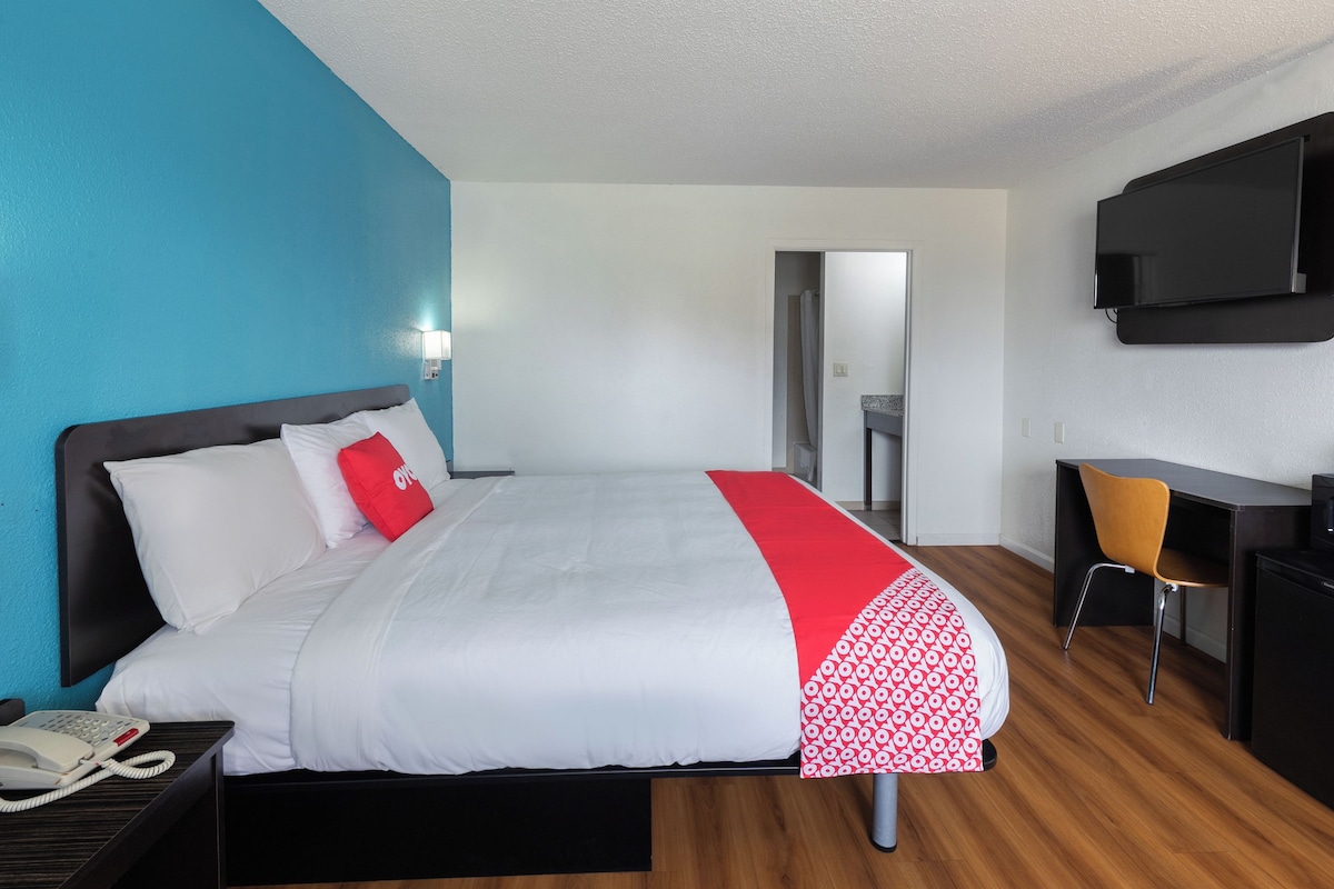 Habitación de hotel con cama, escritorio, silla, televisor y teléfono en la mesita de noche.