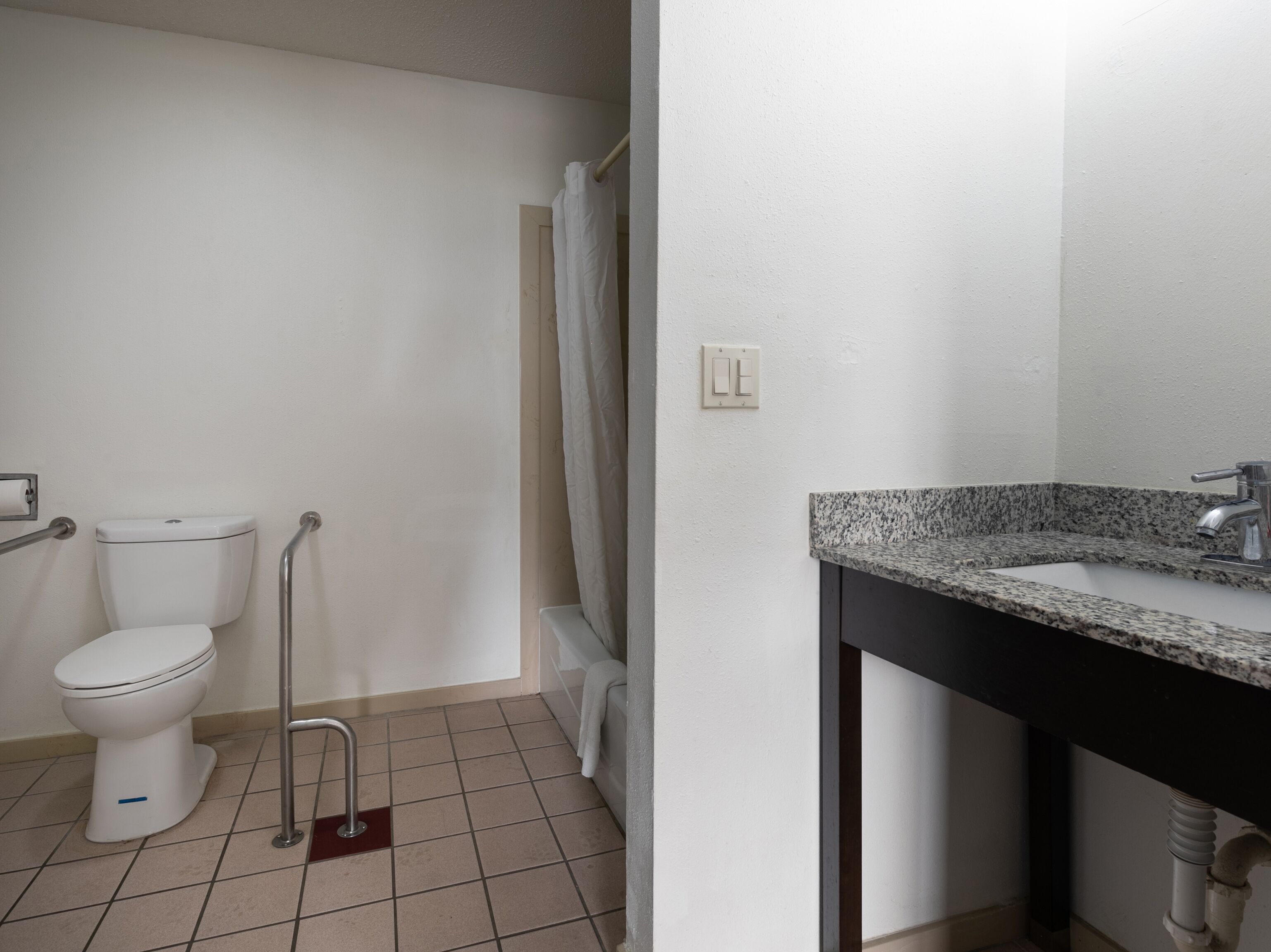 A bathroom with a toilet, grab bars, a shower curtain, a sink with a granite countertop, and a mirror.