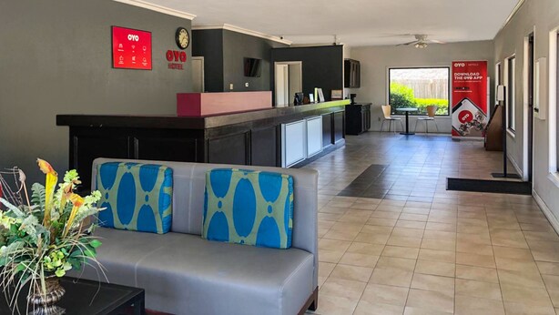 A hotel lobby with a reception desk, a sofa with patterned cushions, a small table, and a decorative plant. - OYO Hotel DeRidder Hwy 171 North (DeRidder)
