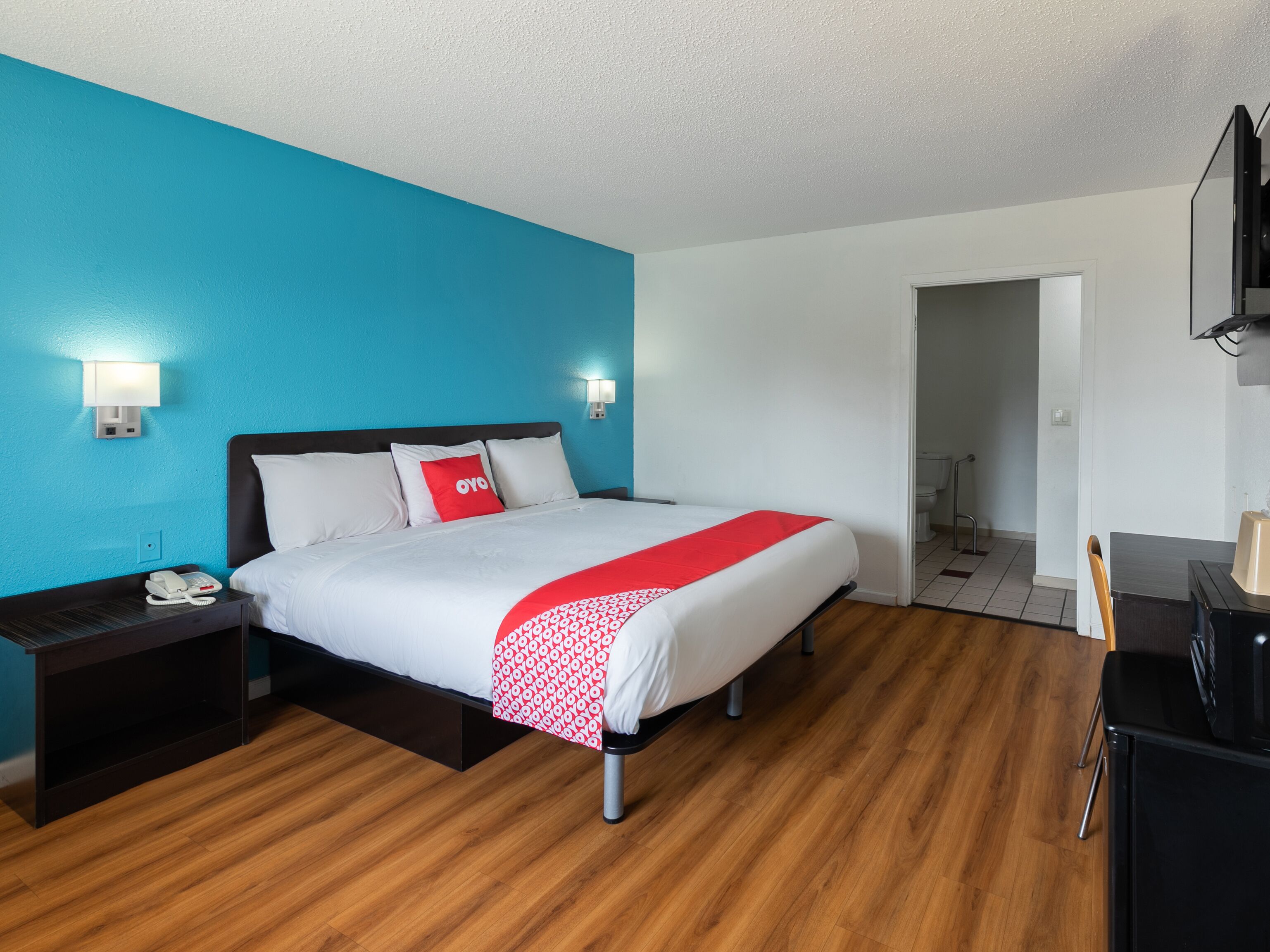 A hotel room with a bed, a nightstand, a desk, and a bathroom visible through an open door.