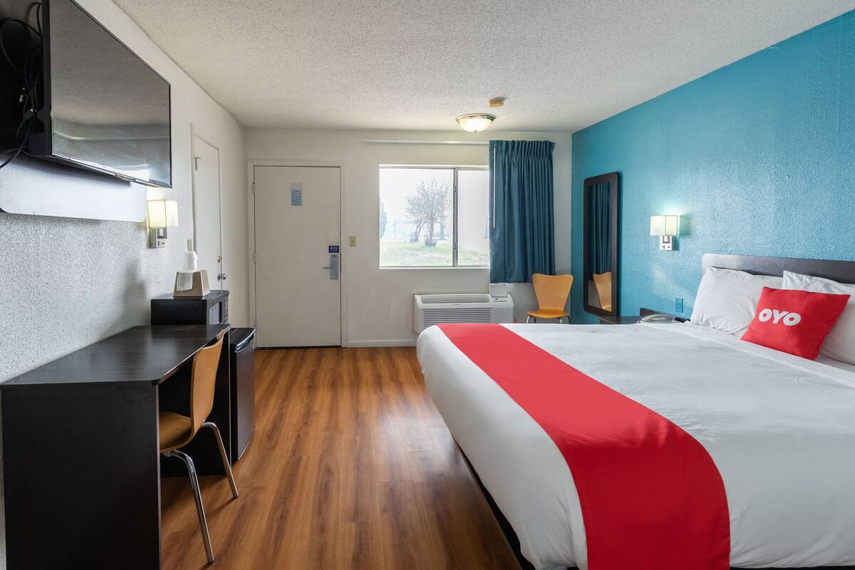 Ein Hotelzimmer mit einem Bett, einem Schreibtisch, einem Sessel, einem Fernseher und einem Vorhangfenster.