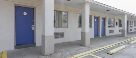 Una fila de habitaciones de hotel con puertas azules, paredes blancas y suelo de concreto.