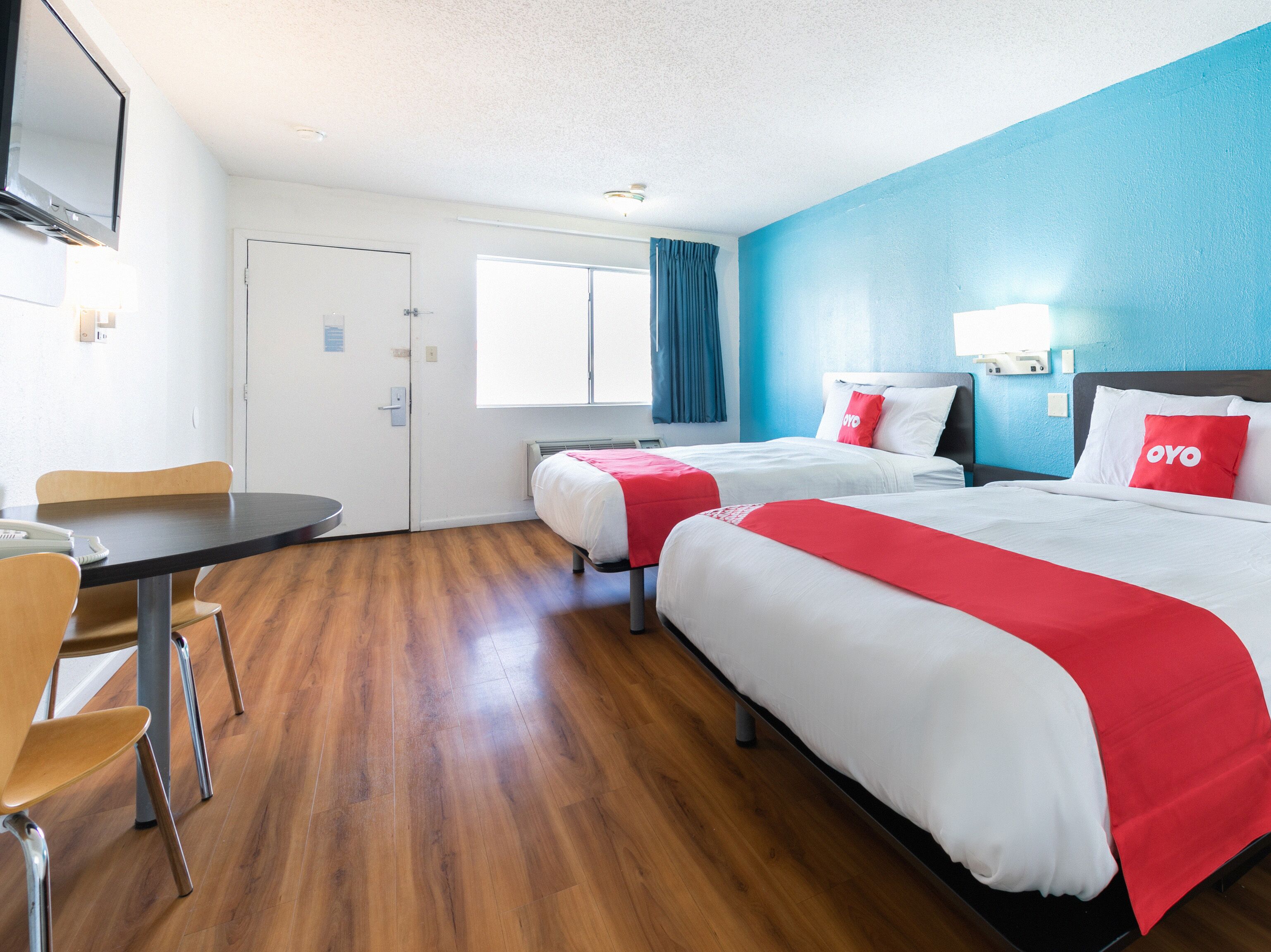 A hotel room with two beds, a dining table, and a TV.