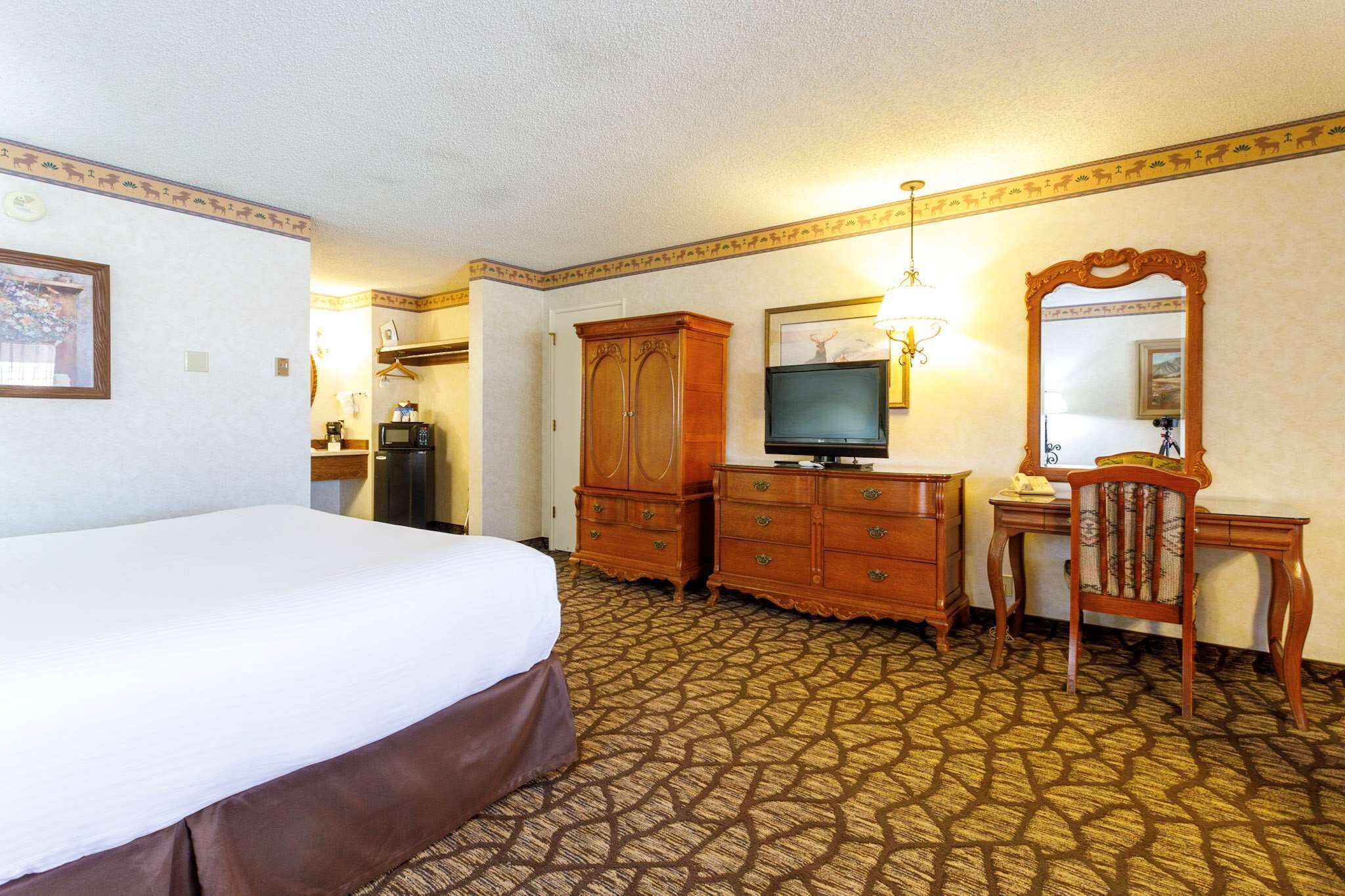Quarto de hotel com uma cama grande, armário de madeira, escrivaninha com cadeira, televisão e espelho.