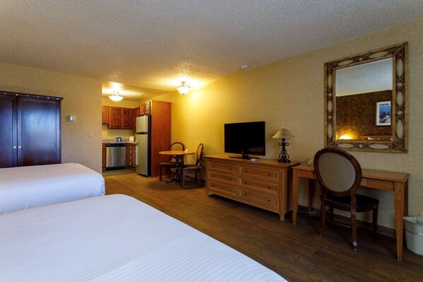 A hotel room with two beds, a desk with a television, a chair, a small table, and a kitchenette in the background. - Gold Country Inn and Casino by Red Lion Hotels (Elko)