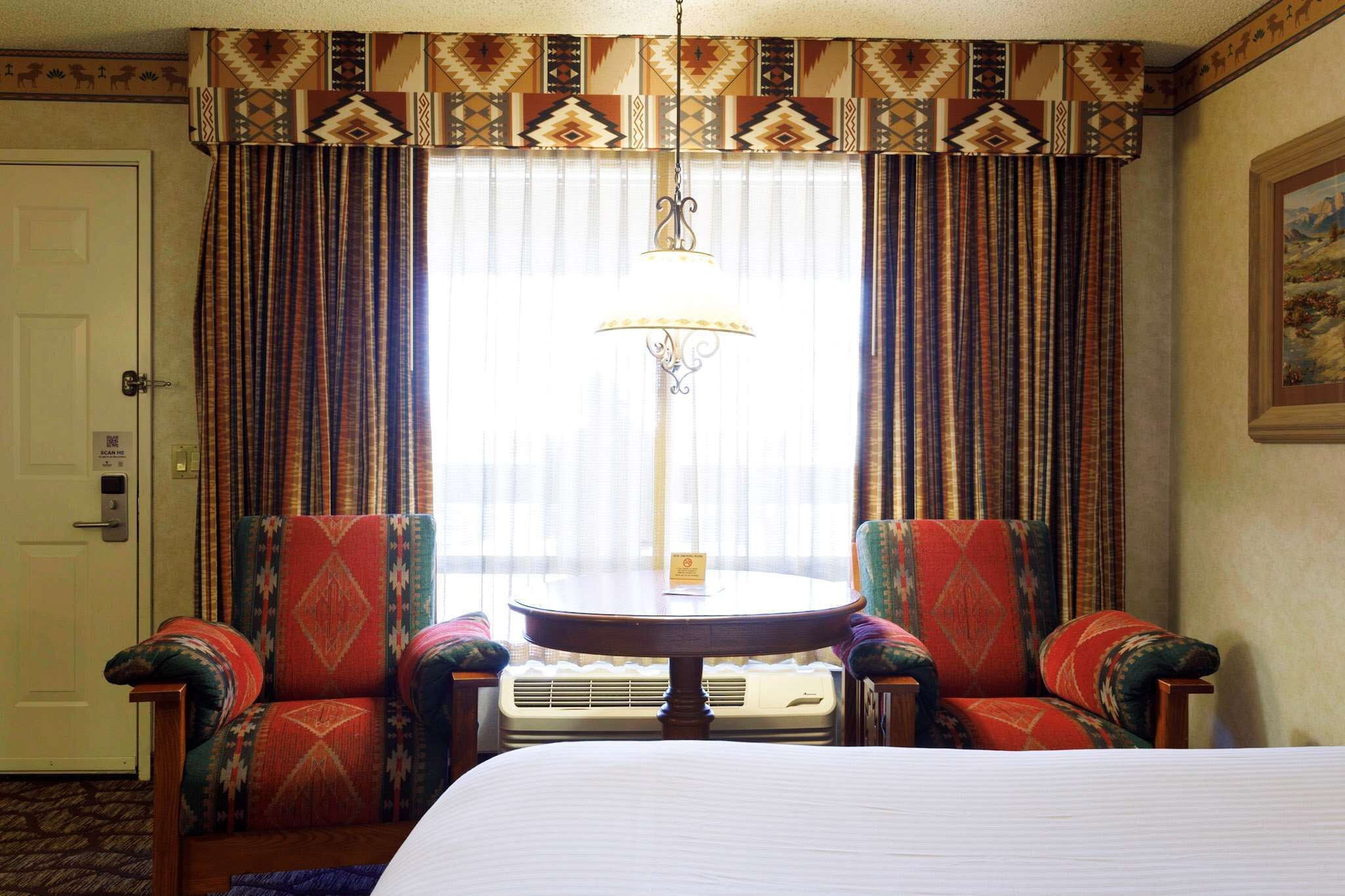 A hotel room with a bed, two armchairs, a round table, and a large window with curtains.