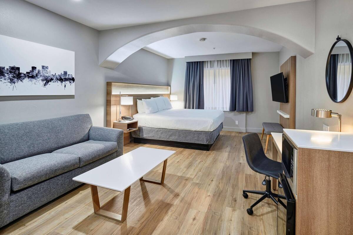 Una camera d'albergo moderna con un letto, un divano, una scrivania e una televisione a schermo piatto.