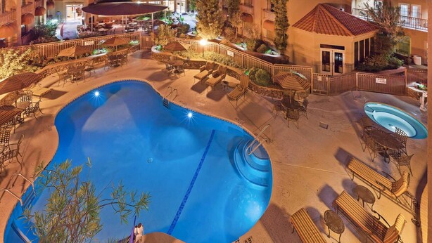 A pool area with lounge chairs and a hot tub, surrounded by a fence and trees. - Radisson Hotel El Paso Airport (El Paso)