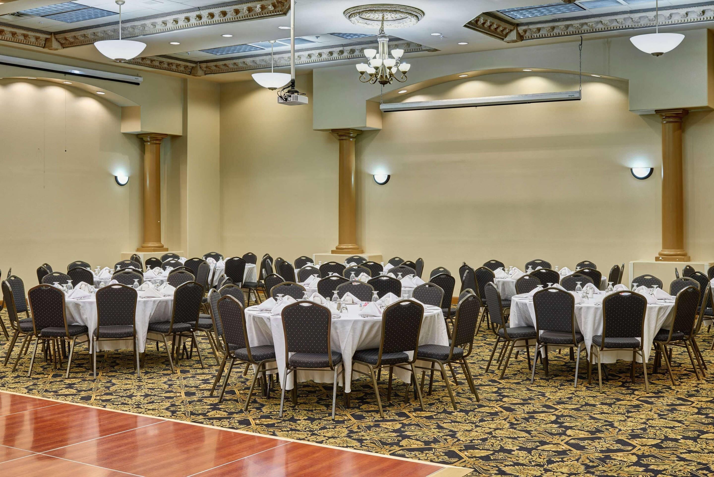 A banquet hall with round tables and chairs, chandeliers, and a patterned carpet.