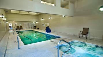 Una piscina interior con agua cristalina, barandales metálicos y una silla de descanso.