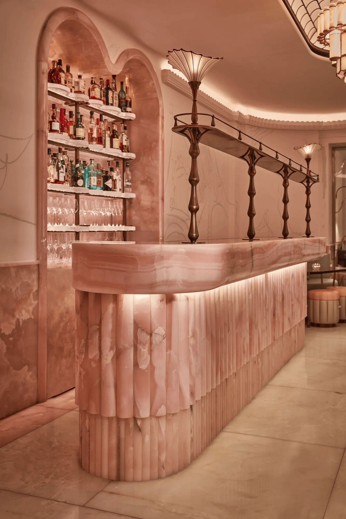 Un espace bar doté d’un comptoir en marbre, d’étagères remplies de bouteilles d’alcool et d’un luminaire décoratif.