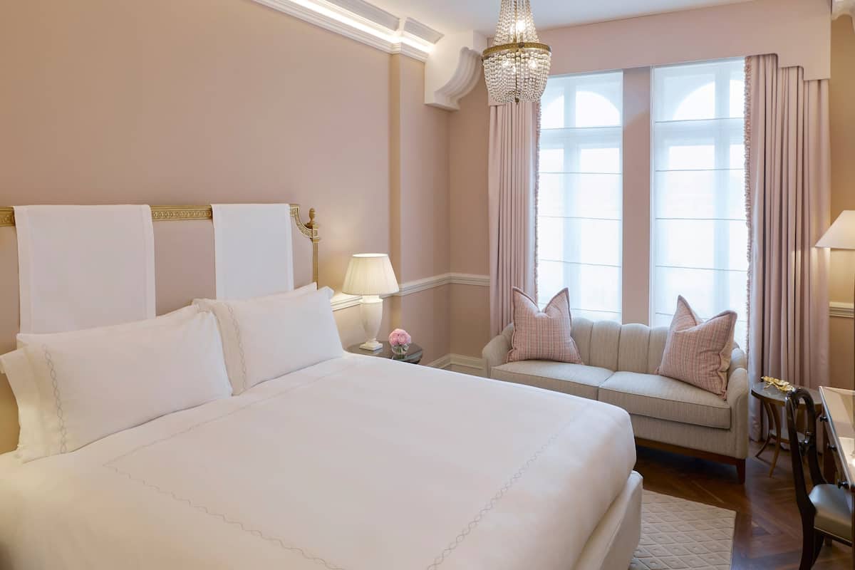 A hotel room with a large bed, a sofa, a chandelier, and a view of the outdoors.