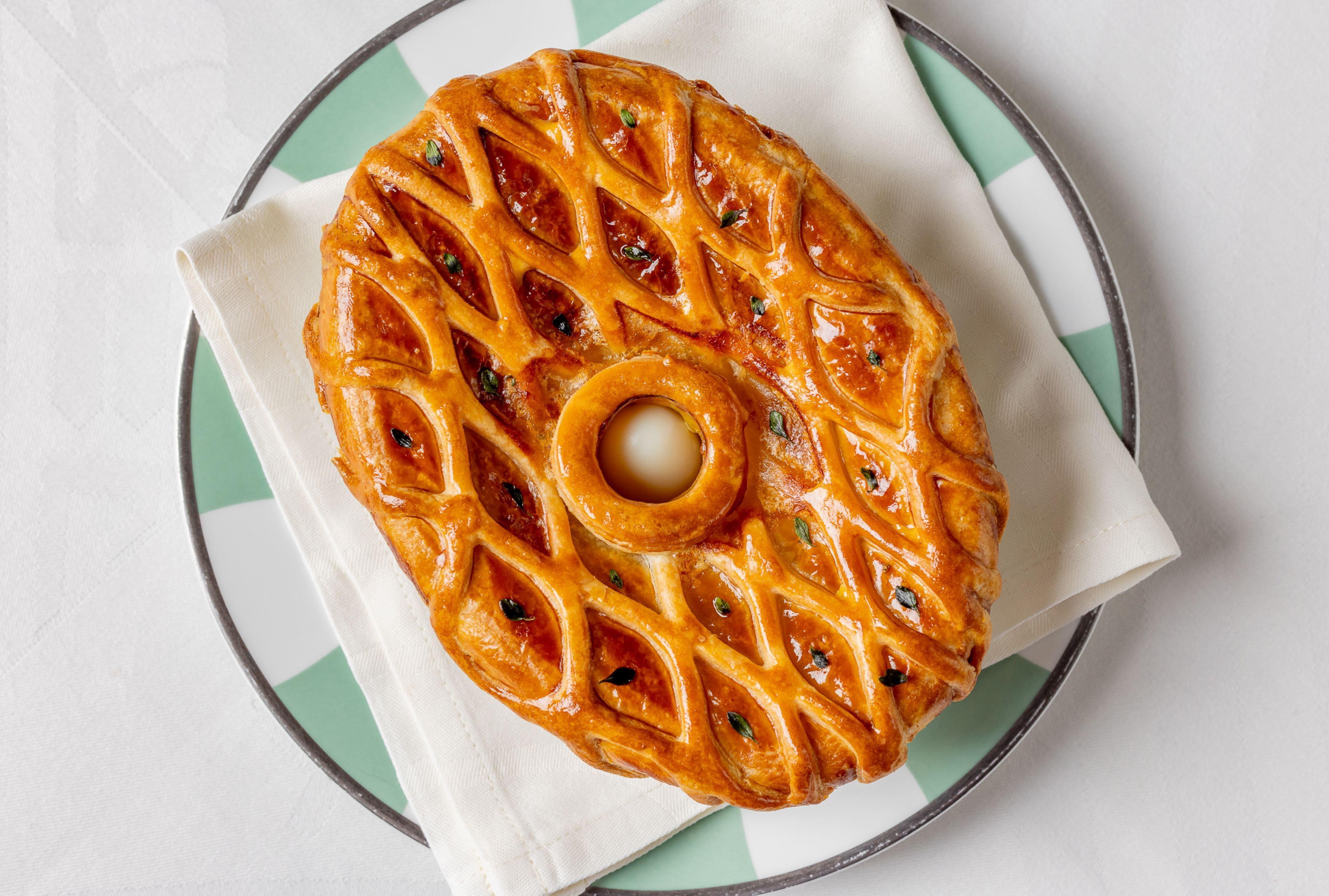 A round pastry with a lattice design on a plate with a green and white pattern.