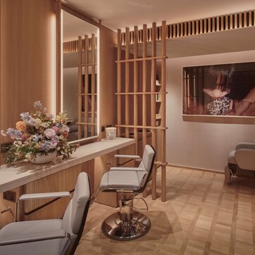 A modern salon with wooden paneling, multiple hairdressing chairs, and a large mirror.