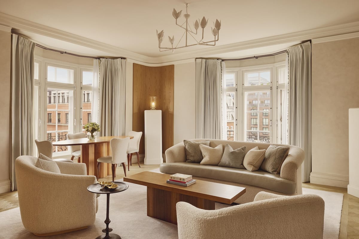 A living room with a sofa, armchairs, a coffee table, a chandelier, and large windows with curtains.
