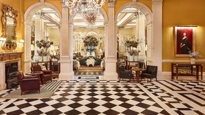 Un hall majestuoso con suelo a cuadros, candelabros ornamentados y muebles clásicos.