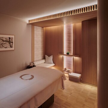 A modern bedroom with a large bed, a bedside table, a small stool, and a wall-mounted shelf.