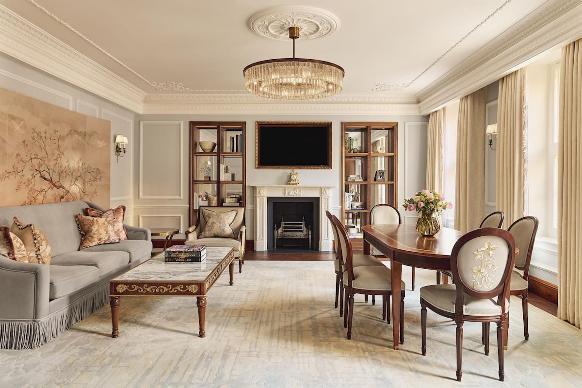 A formal living room with a fireplace, a chandelier, and a dining area with chairs and a table.