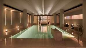 Una amplia piscina interior con un diseño moderno, rodeada de columnas e iluminación suave.
