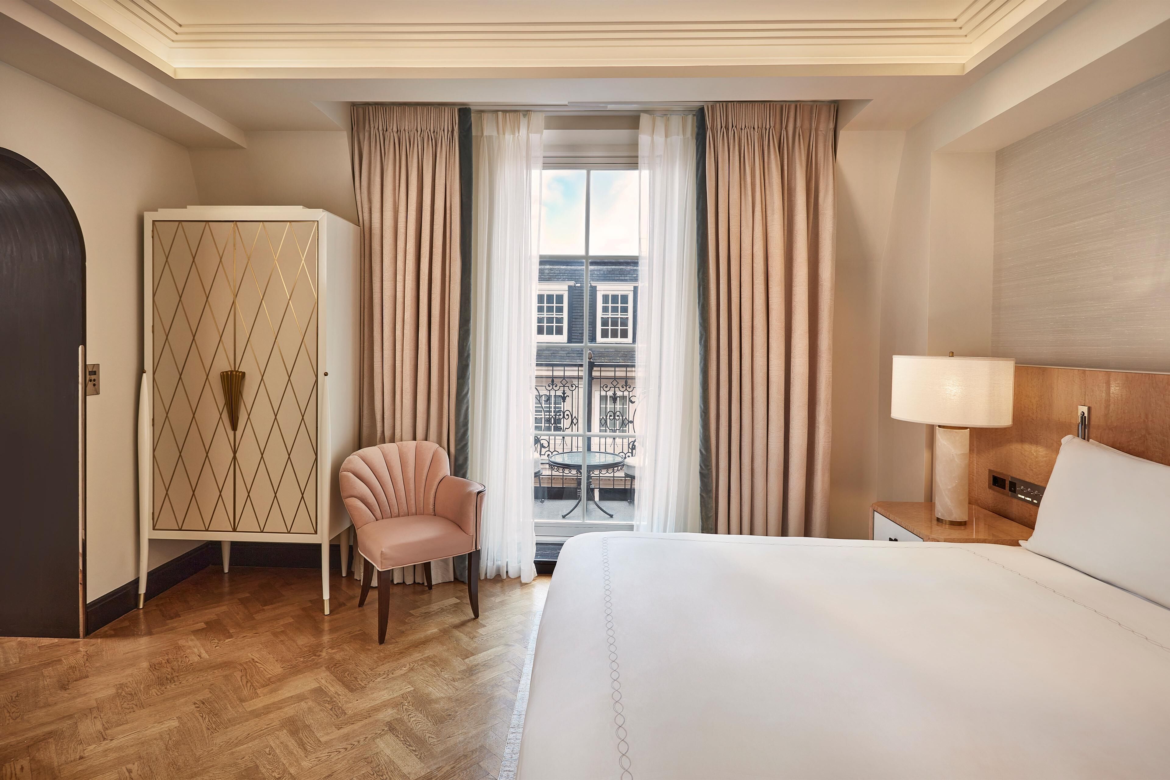 Habitación de hotel con una cama grande, una silla, un armario, una mesita de noche con lámpara y vistas al balcón exterior.