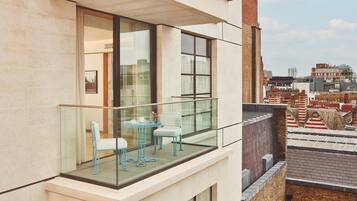 Een balkon met glazen hekwerk, twee stoelen en een klein tafeltje met kop en schotel.