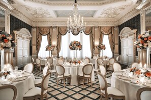 Een statige eetzaal met versierde kroonluchters, weelderige bloemstukken en klassiek meubilair.