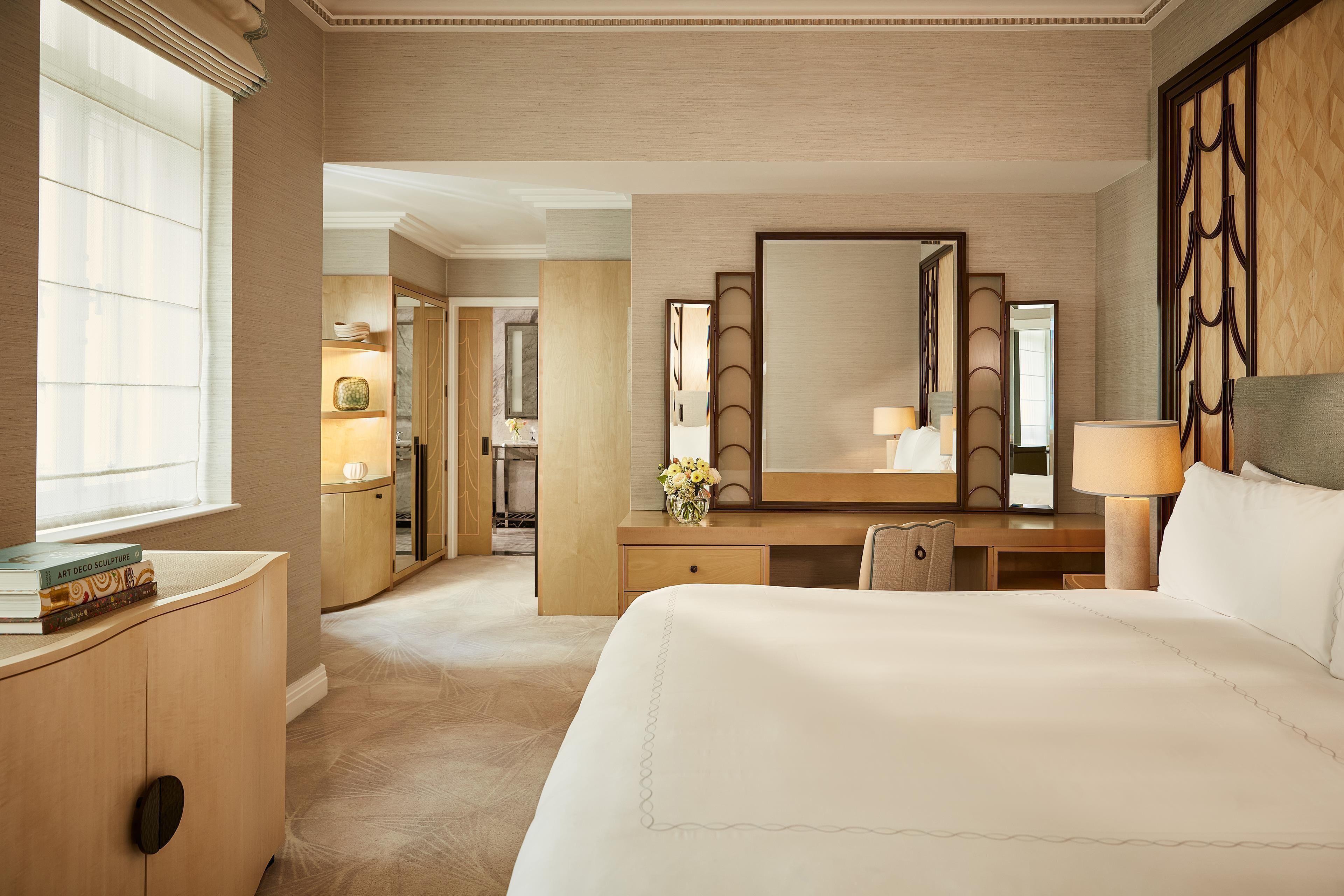 A hotel room with a large bed, a desk with a mirror, a dresser, and a window with blinds.