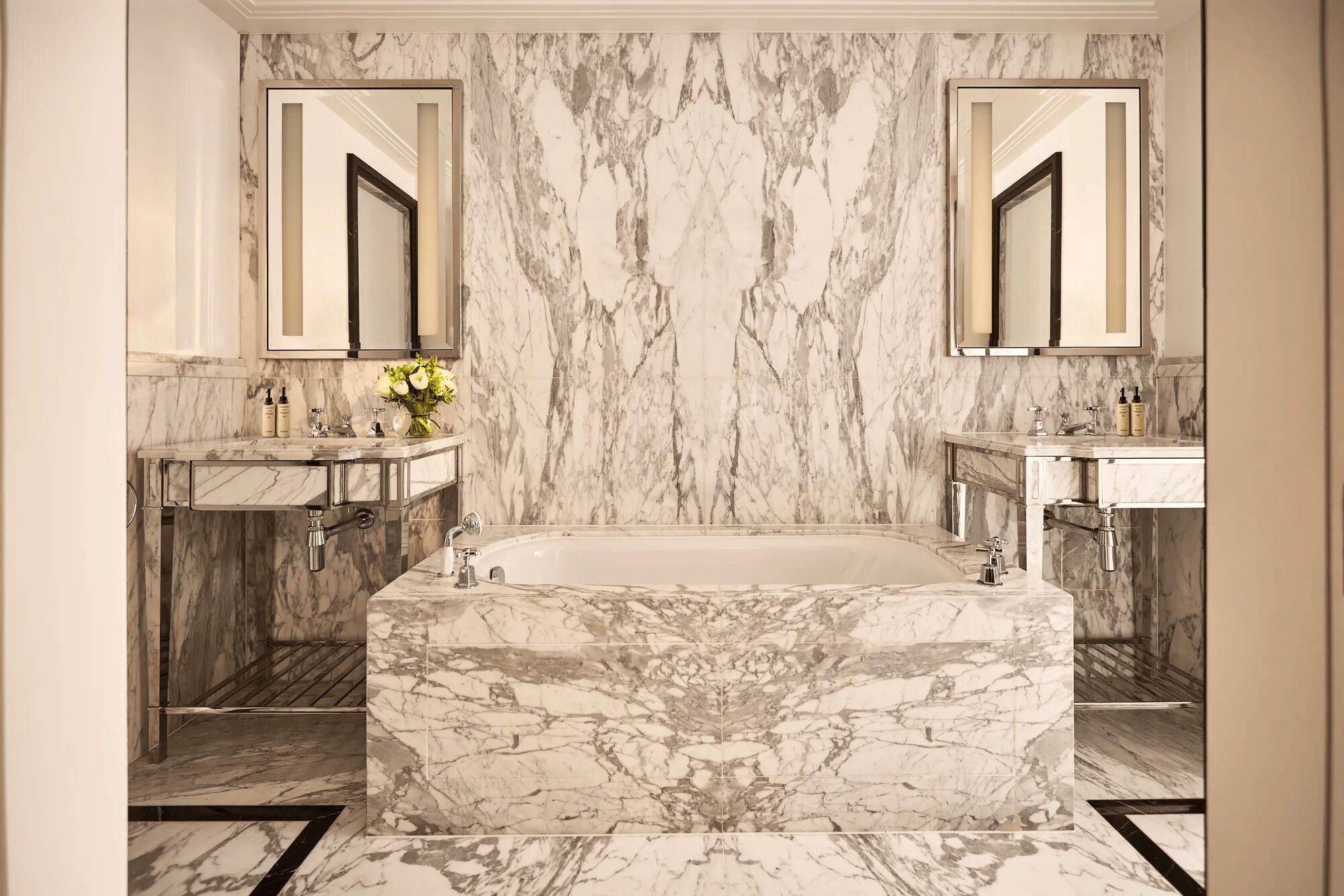 Un baño con piso de mármol, dos lavamanos, una bañera grande y dos espejos.