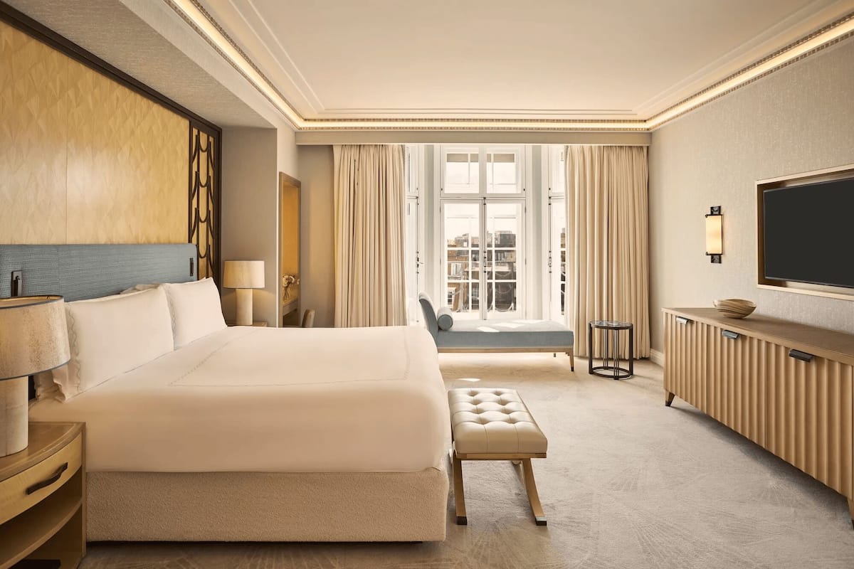 A hotel room with a large bed, a seating area, a television, and a view of the city.