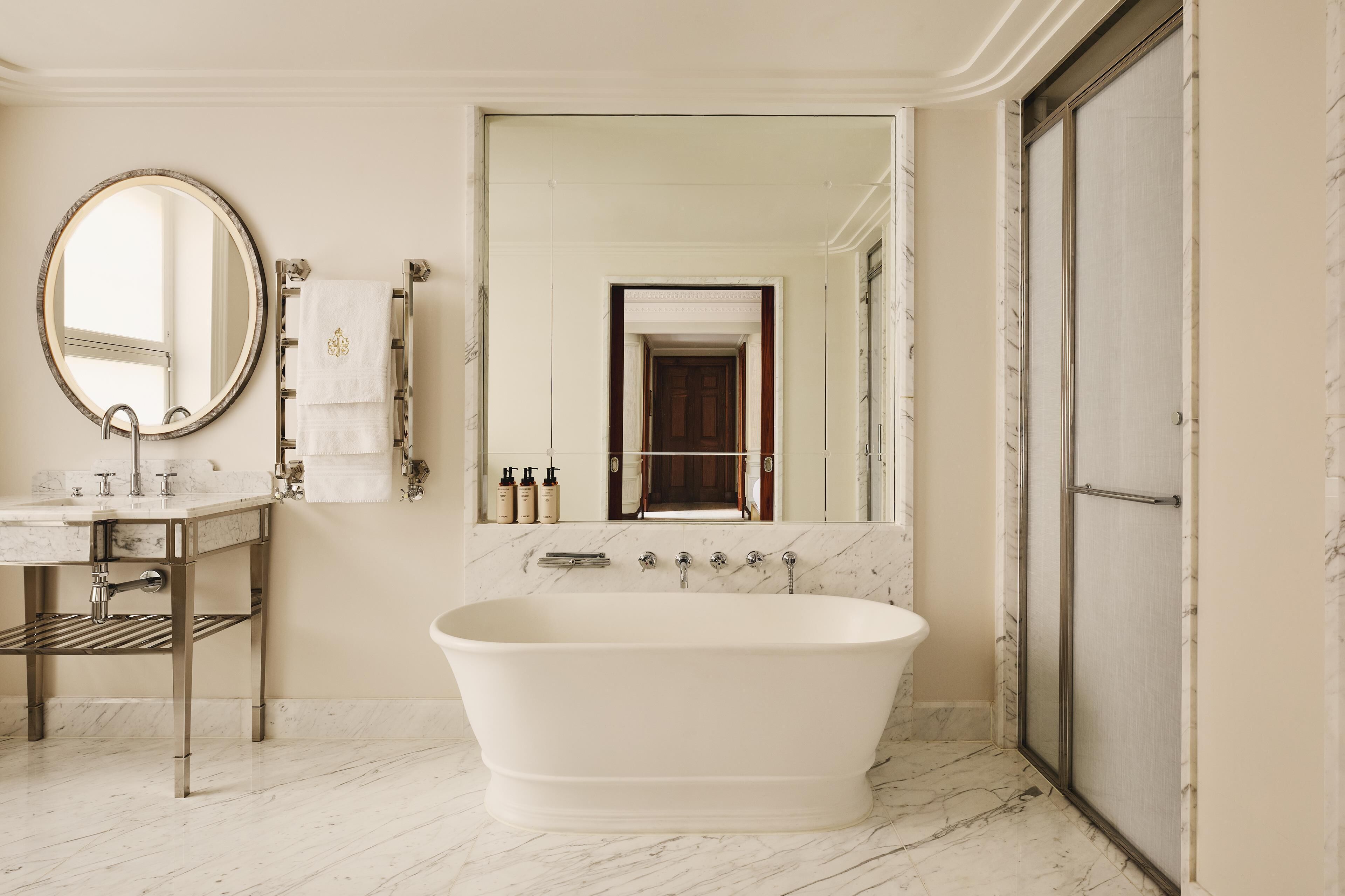 A bathroom with a freestanding bathtub, a round mirror, and a vanity with a marble countertop.