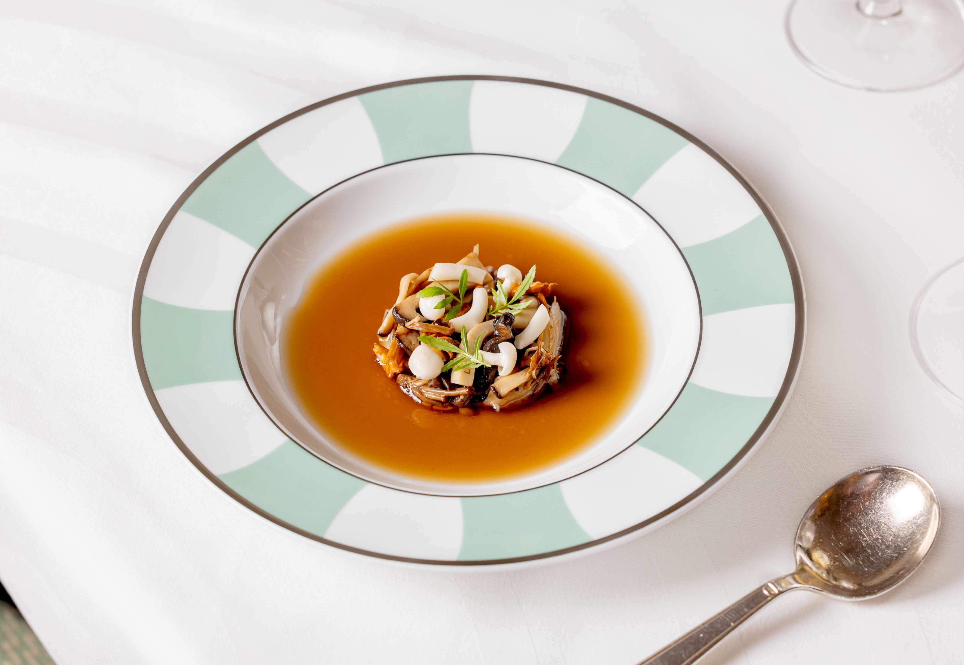 A plate with a food item and a spoon on a white tablecloth.