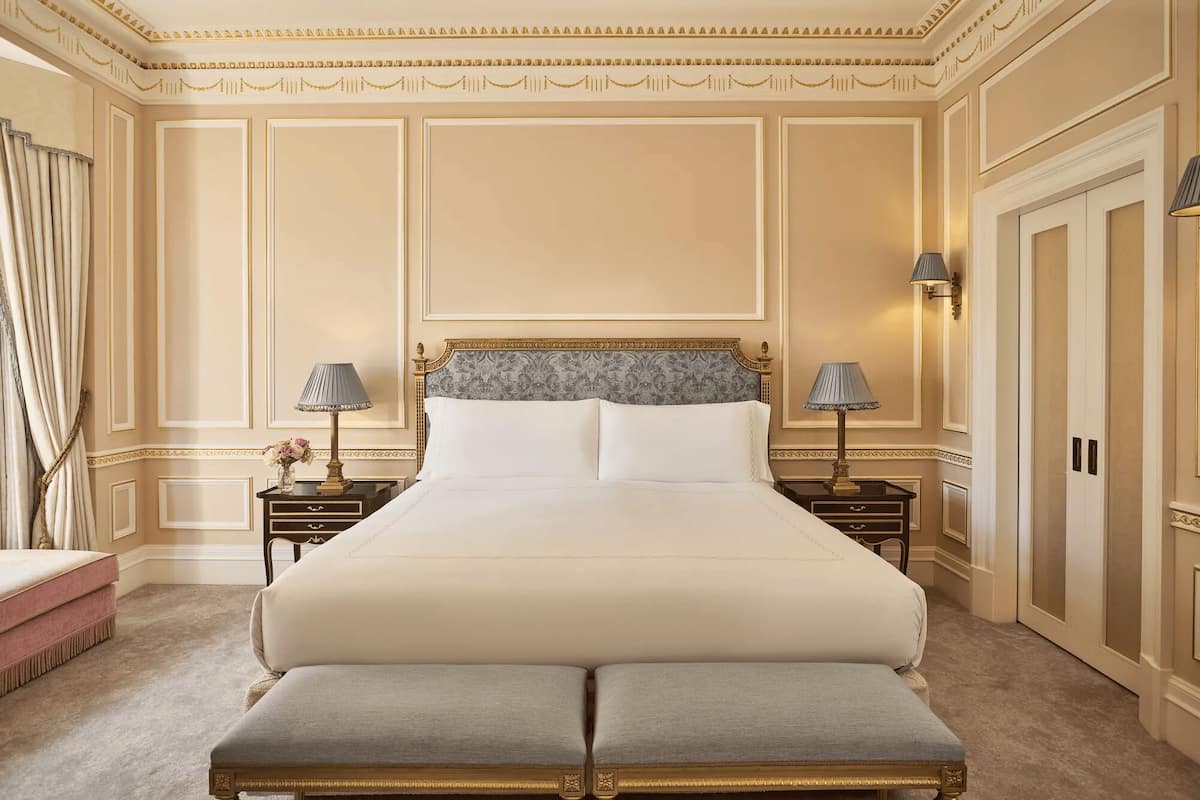 A large bed with a headboard, two bedside tables with lamps, a bench, and a wardrobe.