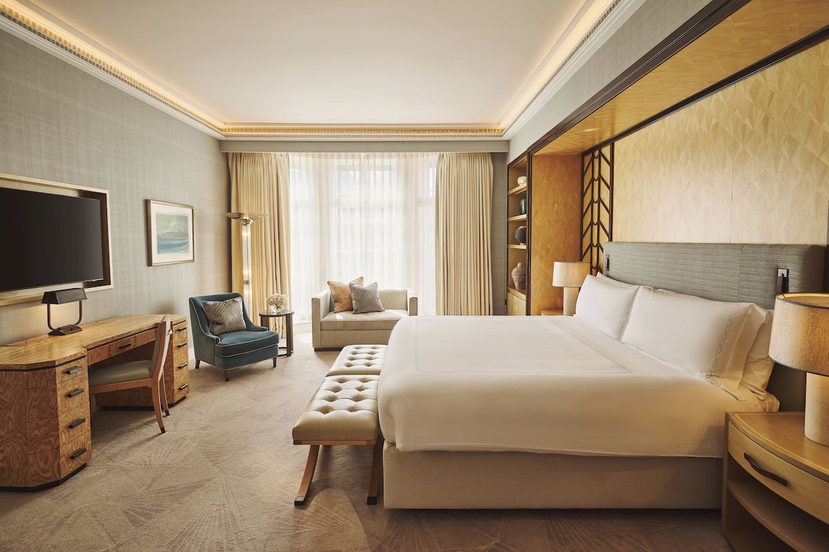 A hotel room with a large bed, a desk with a TV, a chair, a sofa, and a bedside table with a lamp.